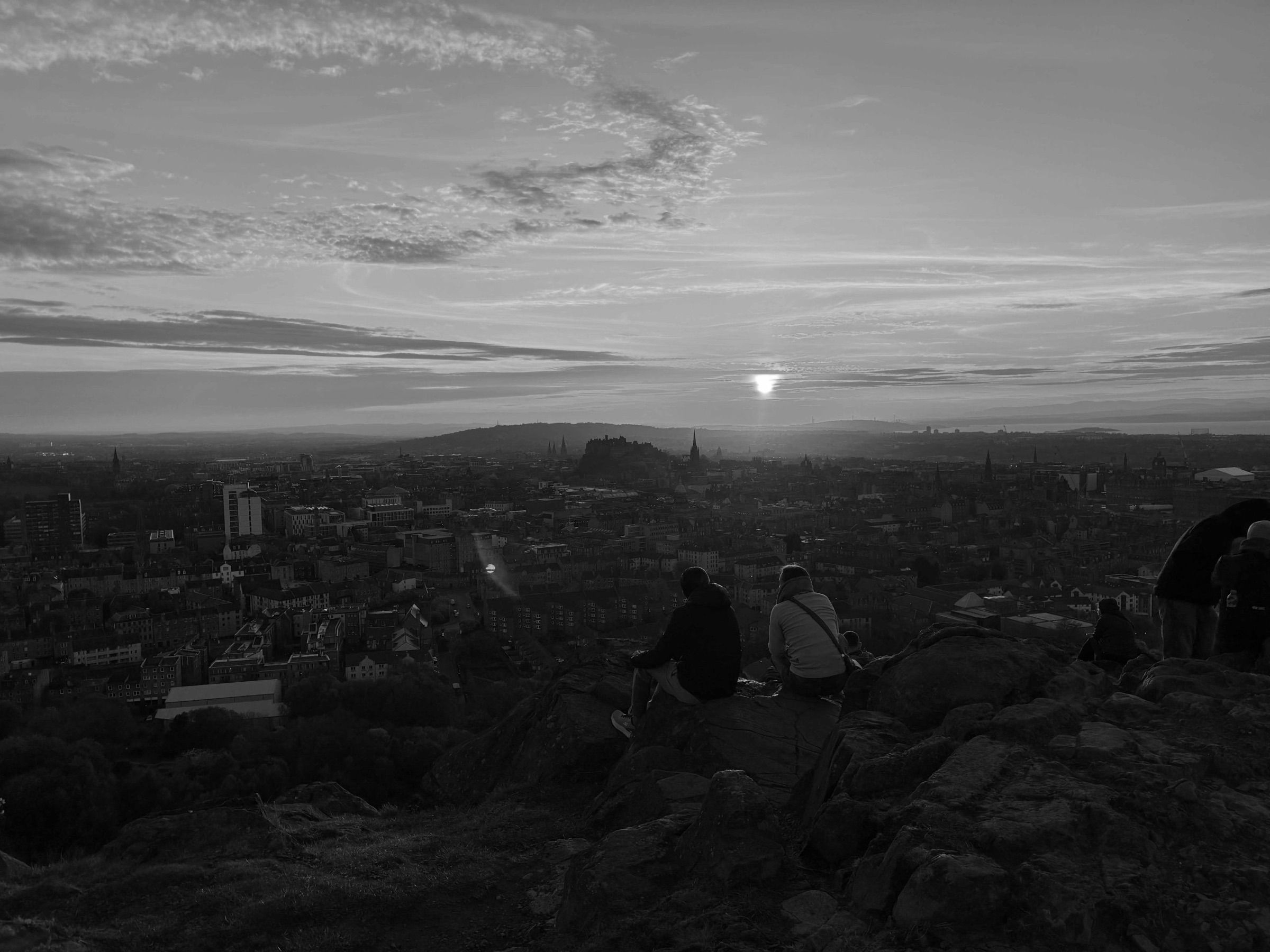 People sitting on the rocks of Arthur’s Seat at sunset, looking out over Edinburgh